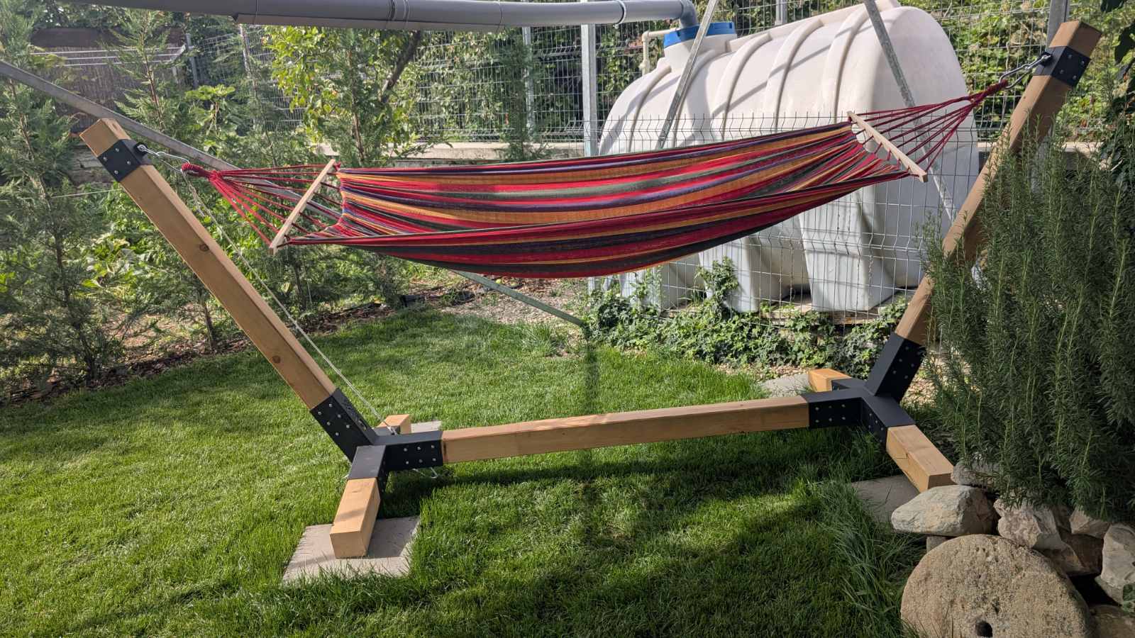 Red and brown striped hammock on a wooden stand in a garden setting